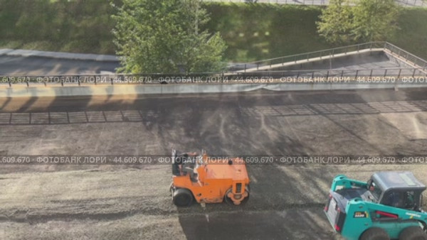 IRKUTSK, RUSSIA - September 06, 2024: Video of road works on the territory adjacent to a high-rise building. One worker brings crushed stone and sand on a loader, another worker compacts the soil with a roller. Редакционное видео, видеограф Виктория Катьянова / Фотобанк Лори