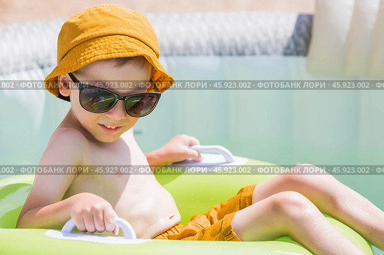 It's a hot day. A cute boy in sunglasses and a panama hat swims on a circle in a foam pool. The concept of summer holidays with children. Стоковое фото, фотограф Photojuli / Фотобанк Лори