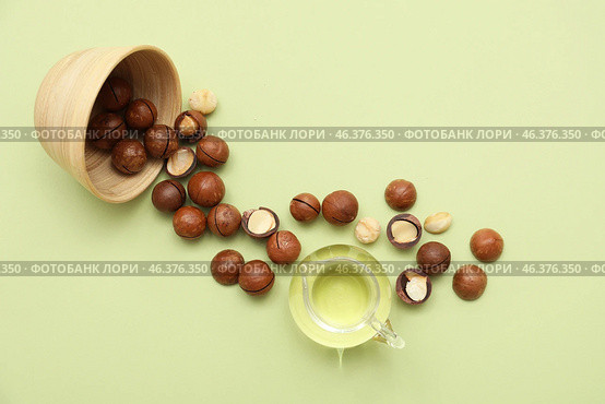 Jug of macadamia oil and overturned bowl with nuts on green background. Стоковое фото, фотограф Pixel_shot / Фотобанк Лори