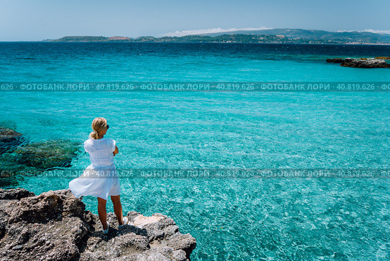 Jung adult women in white dress on summer vacation in front of sea coast landscape of small beach with crystal clear blue water. Greece, Kefalonia. Стоковое фото, фотограф Igor Tichonow / Фотобанк Лори