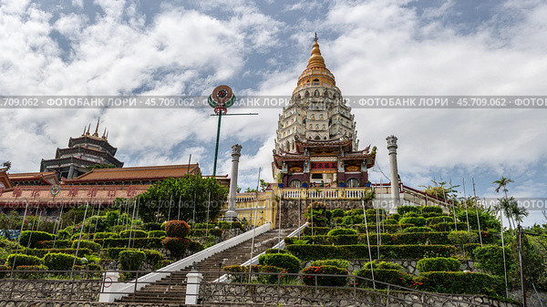Kek Lok Si Temple in Penang, Malaysia featuring stunning pagoda, intricate architecture, lush greenery, grand staircase leading to temple entrance under partly cloudy sky. Стоковое фото, фотограф Павел Муравьев / Фотобанк Лори