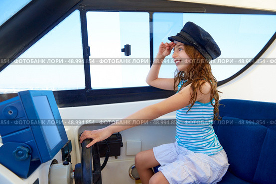 Kid girl pretending be a captain sailor cap in boat indoor holding wheel. Стоковое фото, агентство Ingram Publishing / Фотобанк Лори