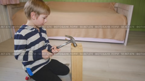 Kid hammers nails to wood with a hammer. Little boy helping with toy tools. Funny 6 years child having fun on building. Kid hammering crafting stuff using wooden pieces. Carpentry and family concept. Стоковое видео, видеограф Марина Демидюк / Фотобанк Лори
