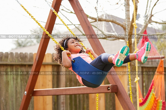 Kid toddler girl swinging on a playground swing in the backyard latin ethnicity. Стоковое фото, агентство Ingram Publishing / Фотобанк Лори