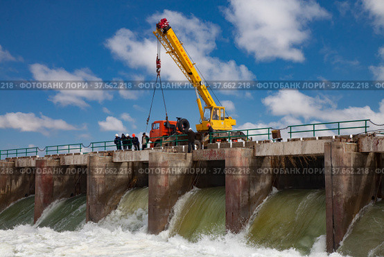 Kok-aral, Kazakhstan - May 03, 2012: Small Aral Sea Kok-aral dam. Water discharge in flood. Open shutters. Yellow mobile crane and workers on dam. Стоковое фото, фотограф Alexey Rezvykh / Фотобанк Лори