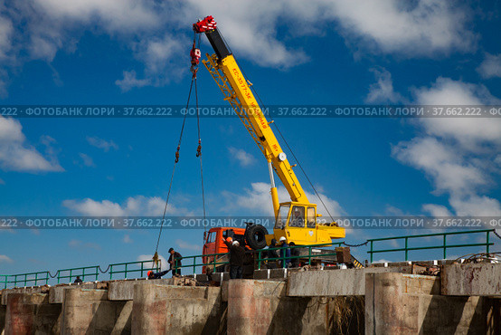 Kok-aral, Kazakhstan - May 03, 2012: Small Aral Sea Kok-aral dam. Mobile crane and workers lifting water shutters in flood. Blue sky, white clouds. Редакционное фото, фотограф Alexey Rezvykh / Фотобанк Лори