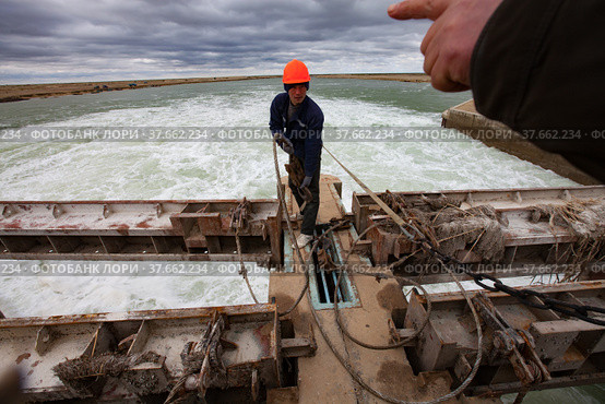 Kok-aral, Kazakhstan - May 03, 2012: Small Aral Sea Kok-aral dam. Worker in orange hardhat use steel rope to lifting water shutter weighting agent. Редакционное фото, фотограф Alexey Rezvykh / Фотобанк Лори