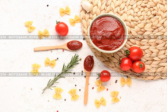 Композиция с плетеной циновкой, миской вкусной томатной пасты и сырой пастой фарфалле на белом гранж-фоне. Стоковое фото, фотограф Pixel_shot / Фотобанк Лори