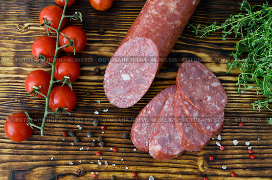 Копчёная колбаса, нарезанная ломтиками,  с овощами и специями на разделочной доске. Стоковое фото, фотограф Snezka / Фотобанк Лори