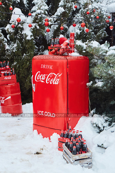Krasnodar, Russia - December 10, 2021: Coca-Cola refrigerator on the street during snow and various products of this company. A photo zone for creating a Christmas mood. Редакционное фото, фотограф Наталия Кирсанова / Фотобанк Лори