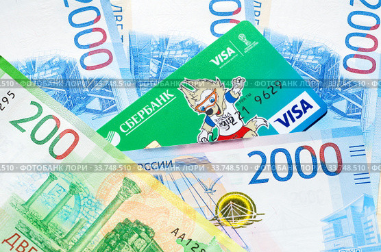 Кредитная карта Visa с Забивакой - талисманом Чемпионата мира по футболу FIFA лежит на новых денежных купюрах (2018 год). Редакционное фото, фотограф Елена Коромыслова / Фотобанк Лори