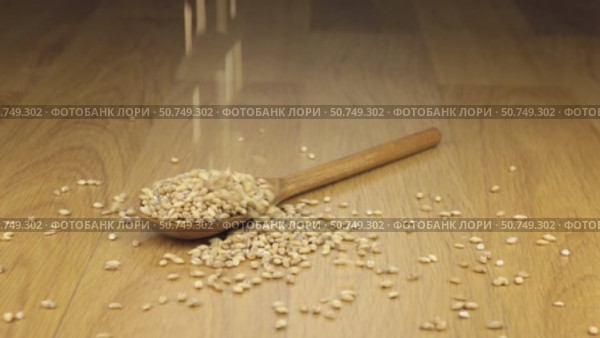 Крупинки перловой крупы сыплются на деревянную ложку, лежащую на деревянной поверхности. История приготовления. Стоковое видео, видеограф Александр Собко / Фотобанк Лори
