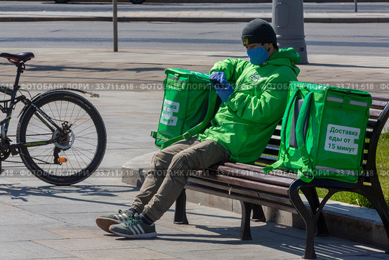 Курьер сервиса доставки еды Delivery Club принимает заказ в парке в центре города Москвы во время эпидемии коронавируса COVID-19 в Россия (2020 год). Редакционное фото, фотограф Николай Винокуров / Фотобанк Лори