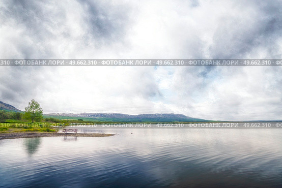 Lake scenery with a bench and a pine tree near the calm water and mountains in the background. Стоковое фото, агентство Ingram Publishing / Фотобанк Лори