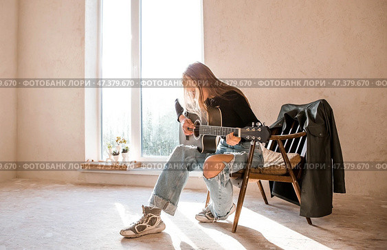 Learning to play the guitar. Music. A talented girl musician sits alone and plays songs on the guitar. The girl plays a calm melody on a musical instrument. Стоковое фото, фотограф Photojuli / Фотобанк Лори