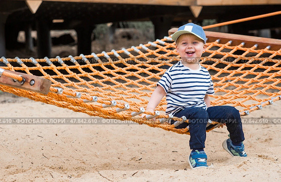 Lifestyle. A cute little boy is sitting in a hammock on a modern outdoor playground. The concept of family entertainment and leisure. Стоковое фото, фотограф Photojuli / Фотобанк Лори