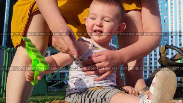 Little baby learns to play with sand in a children's sandbox under the control of a mother woman. Kid aged one year. Стоковое видео, видеограф Андрей Журавлев / Фотобанк Лори