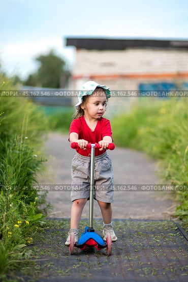 Little girl on scooter with scraped knees on walk. Стоковое фото, фотограф Анна Никонорова / Фотобанк Лори