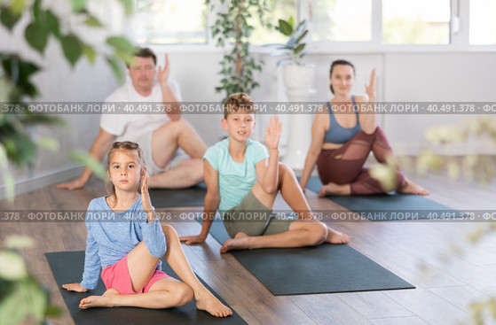 Little girl performs Lord of fish Ardha Matsyendrasana asana, family in background. Стоковое фото, фотограф Яков Филимонов / Фотобанк Лори