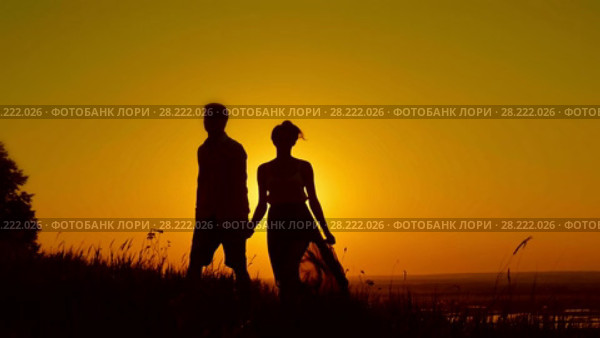 Loving couple - young man and beautiful girl walking at sunset meadow - silhouette. Стоковое видео, видеограф Константин Шишкин / Фотобанк Лори