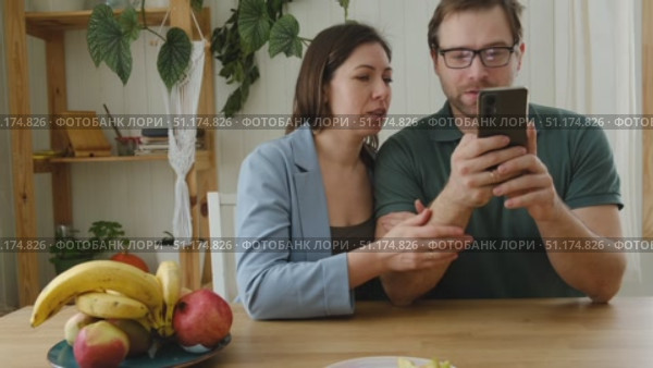 Loving mature couple using mobile phone. Husband and wife hugging, holding hands and looking at the smartphone screen. Man and woman share content on social media app. Young people watch the cellphone. Стоковое видео, видеограф Марина Демидюк / Фотобанк Лори