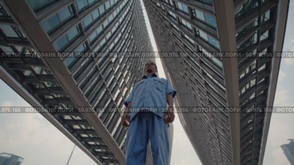 Low angle view of a determined laborer standing among towering modern buildings, illustrating the contrast between urban development and the social class divide. Стоковое AI-видео, аниматор Данил Руденко / Фотобанк Лори