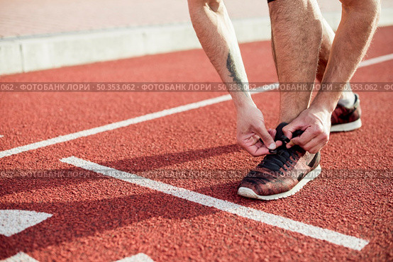 low section male athlete start line tying his shoelace running track. Стоковое фото, агентство Ingram Publishing / Фотобанк Лори