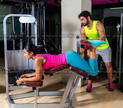 Lying hamstring curl machine girl with personal trainer man. Стоковое фото, агентство Ingram Publishing / Фотобанк Лори