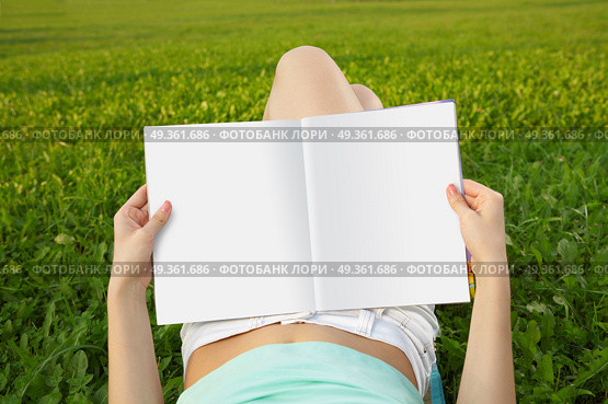 Magazine of in a lap reading person against a field. Rest with reading . Стоковое фото, агентство Ingram Publishing / Фотобанк Лори