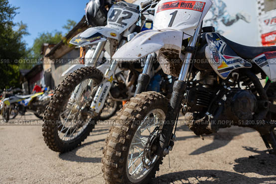 Magnitogorsk, Russian Federation - August 23, 2025: Enduro motorcycles lined up in a dirt competition area, showcasing rugged tires and vibrant designs, ready for thrilling races and adventure. Редакционное фото, фотограф Ирина Ручушкина / Фотобанк Лори