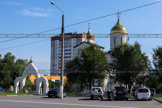 Magnitogorsk, Russian Federation - August 24, 2025: Church of the Intercession of the Most Holy Theotokos with golden domes and modern buildings in the background, showcasing urban architecture and spiritual significance. Редакционное фото, фотограф Ирина Ручушкина / Фотобанк Лори