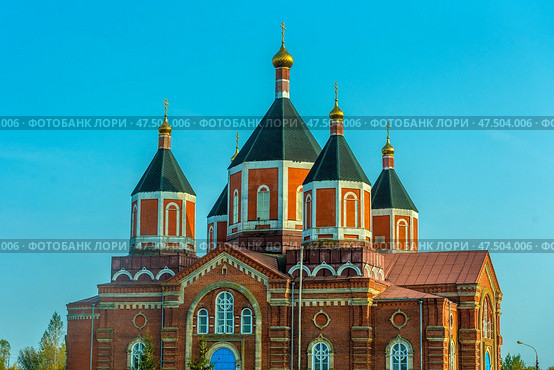 Majestic Orthodox church - Iverskaya Church, located in the village of Borshchevoe, Venevsky district. The building is made of red brick and decorated with white decorative elements. The temple has several high octagonal domes with golden crosses, covered with a dark roof. The central entrance stands out with a bright blue door, and a wide staircase leads to it. The architecture is distinguished by harmonious proportions and classical Russian church style. In the background is a clear blue sky, emphasizing the monumentality of the building. (2020 год). Редакционное фото, фотограф Анна Кривицкая / Фотобанк Лори