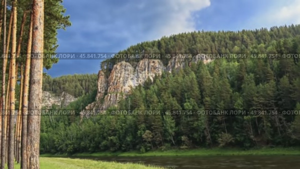 Majestic river flows near pine forest and rocky cliff under cloudy sky. Стоковое AI-видео, аниматор Юрий Поздников / Фотобанк Лори