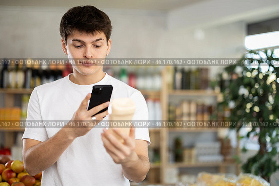 Male buyer checks suitability - scans QR code on jar of mayonnaise label in grocery store. Стоковое фото, фотограф Яков Филимонов / Фотобанк Лори