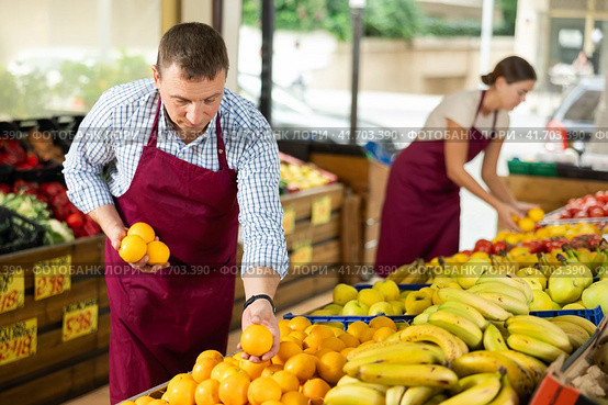 Male seller of vegetable department of store is replenishing showcase with oranges. Стоковое фото, фотограф Яков Филимонов / Фотобанк Лори