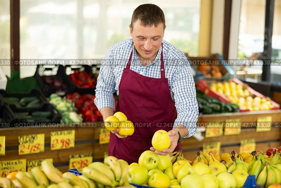 Male seller of vegetable department of store replenishing showcase with apple, put ones on showcase. Стоковое фото, фотограф Яков Филимонов / Фотобанк Лори