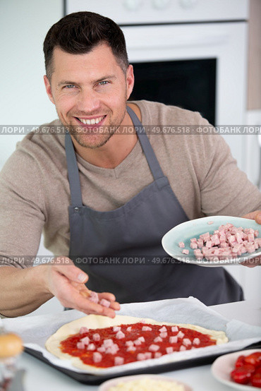 man adds ham topping to homemade pizzaman. Стоковое фото, агентство Ingram Publishing / Фотобанк Лори