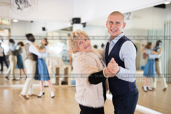 Man and elderly woman performing ballroom dance in dancing room. Стоковое фото, фотограф Татьяна Яцевич / Фотобанк Лори