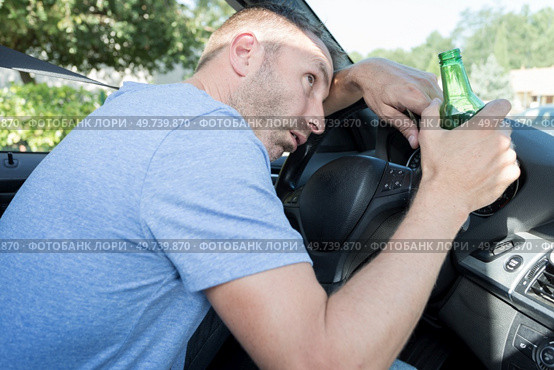 man holding bottle of beer slumped over car steering wheel. Стоковое фото, агентство Ingram Publishing / Фотобанк Лори