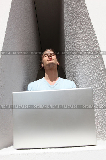 Man in an alcove basking in the sunshine whilst using a laptop. Стоковое фото, агентство Ingram Publishing / Фотобанк Лори