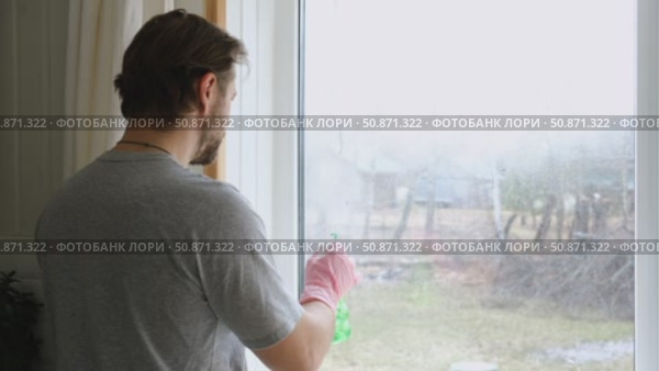 Man is cleaning window in apartment. Adult Male cleaner using a squeegee to wash a window. Bearded guy wiping and washing glasses with with spray bottle, rag and vacoom. Everyday chores. Purification. Стоковое видео, видеограф Марина Демидюк / Фотобанк Лори