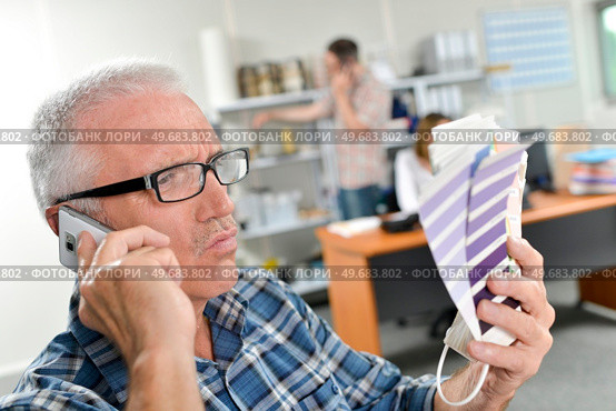 Man on telephone holding colour charts, looking skeptical. Стоковое фото, агентство Ingram Publishing / Фотобанк Лори