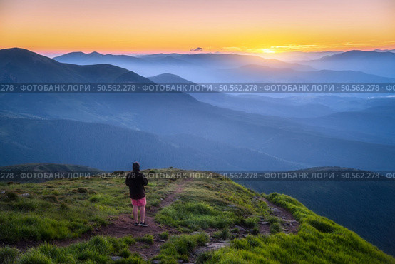 Man on the top of mountain Goverla, Ukraine. Hill with green grass and beautiful mountain valley at sunset in summer. Landscape with sporty man, hils in fog, orange sky. Hiking. Spring in Europe. Стоковое фото, агентство Ingram Publishing / Фотобанк Лори