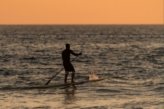Man paddleboarding in open water at sunset. Стоковое фото, агентство Ingram Publishing / Фотобанк Лори
