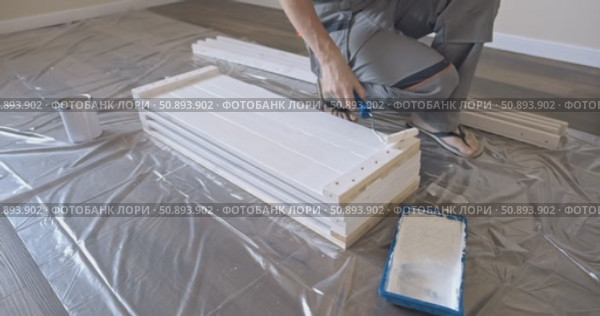 Man Professional carpenter painting wooden boards with white paint using roller brush in modern interior room during home renovation construction. Painting of wooden shelving. furniture assembly. Стоковое видео, видеограф Сергей Тимофеев / Фотобанк Лори