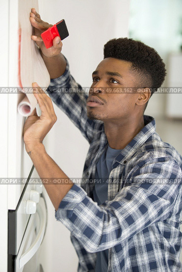 man revamping kitchen unit with adhesive material. Стоковое фото, агентство Ingram Publishing / Фотобанк Лори