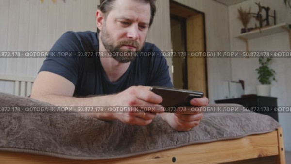 Man using his cellphone. Handsome guy use mobile phone at home. Male browses social networks, gaming, does shopping online, chats with friends, writes or reads messages. Close up. 4k video footage. Стоковое видео, видеограф Марина Демидюк / Фотобанк Лори