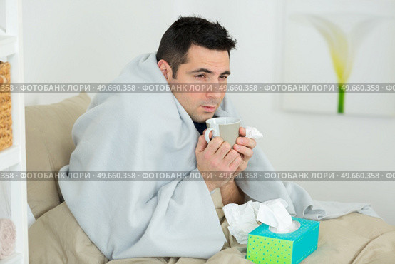 man wrapped in blanket holding hot drink and tissues. Стоковое фото, агентство Ingram Publishing / Фотобанк Лори