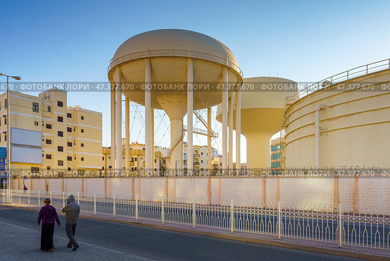 Manama, Bahrain - Jan 08 2024, a Panoramic view of two large beige water towers, a couple of people are walking in the foreground, in the daytime, Manama, Bahrain. Стоковое фото, фотограф Сергей Богомяко / Фотобанк Лори