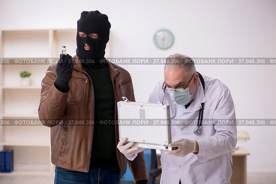 Masked man burglar bribing old doctor for getting vaccine. Стоковое фото, фотограф Elnur / Фотобанк Лори